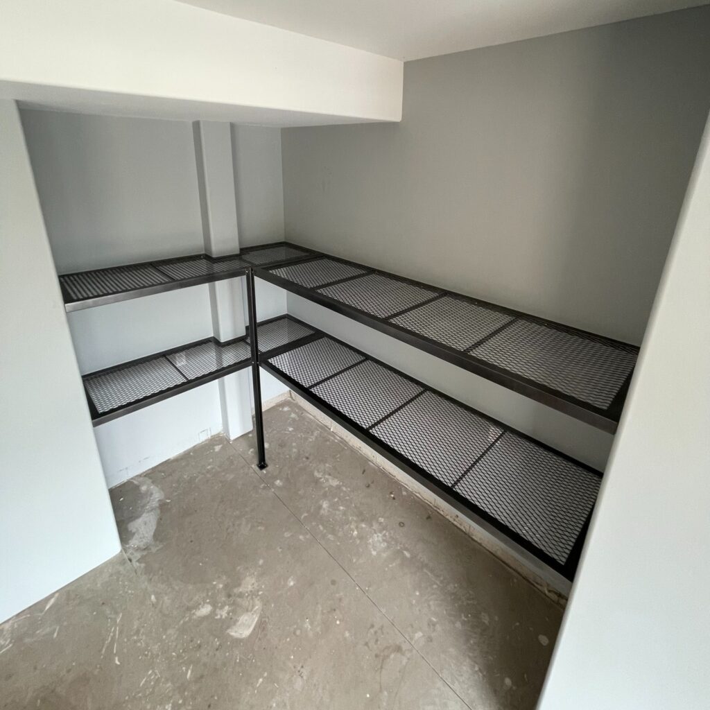 Custom fabricated metal garage shelving by Dream Ironwork featuring laser-cut shelf patterns and a durable gunmetal grey powder-coated finish for heavy-duty storage and modern industrial style.