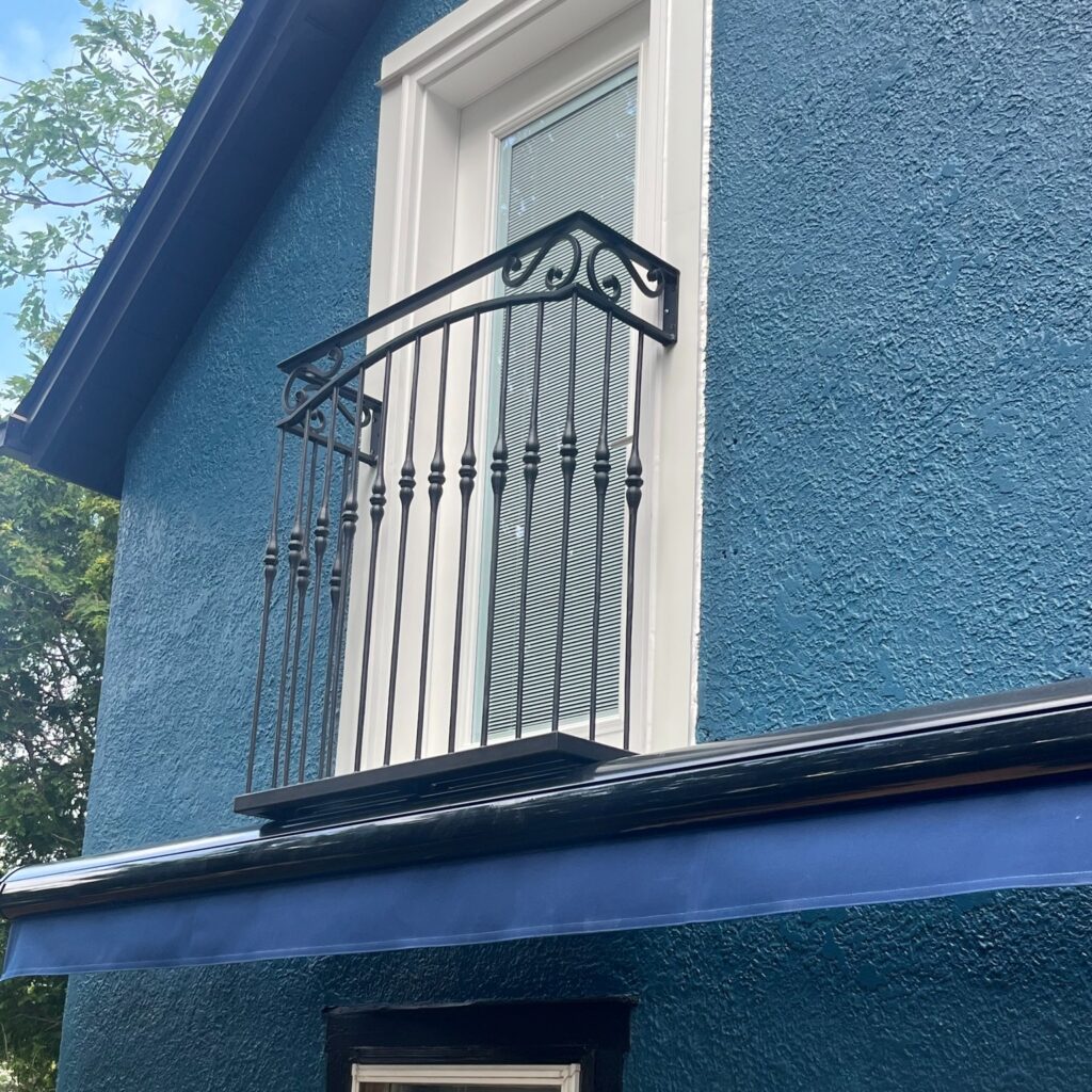 Black decorative iron security bars on a window against a brick wall. Juliet Balcony contractor in Niagara. Juliet Balcony. Juliet Balcony company. Wrought Iron Juliet Balcony.