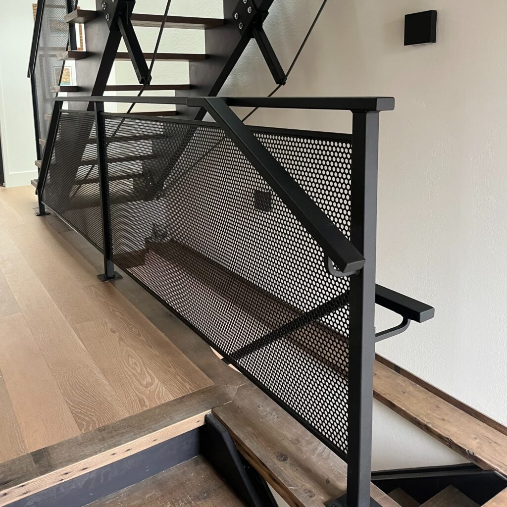 Custom fabricated interior railing by Dream Ironwork featuring a tight laser-cut mesh panel with circular cutout design and seamlessly connected handrails transitioning down into the basement for a smooth, modern finish.