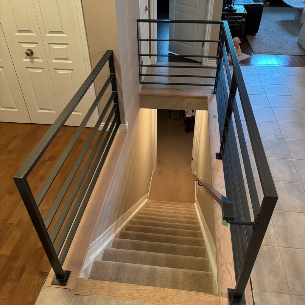 Custom fabricated interior modern horizontal-bar iron railing with integrated handrail leading to the basement by Dream Ironwork, featuring precision welding, clean contemporary lines, and durable craftsmanship for residential safety and style.