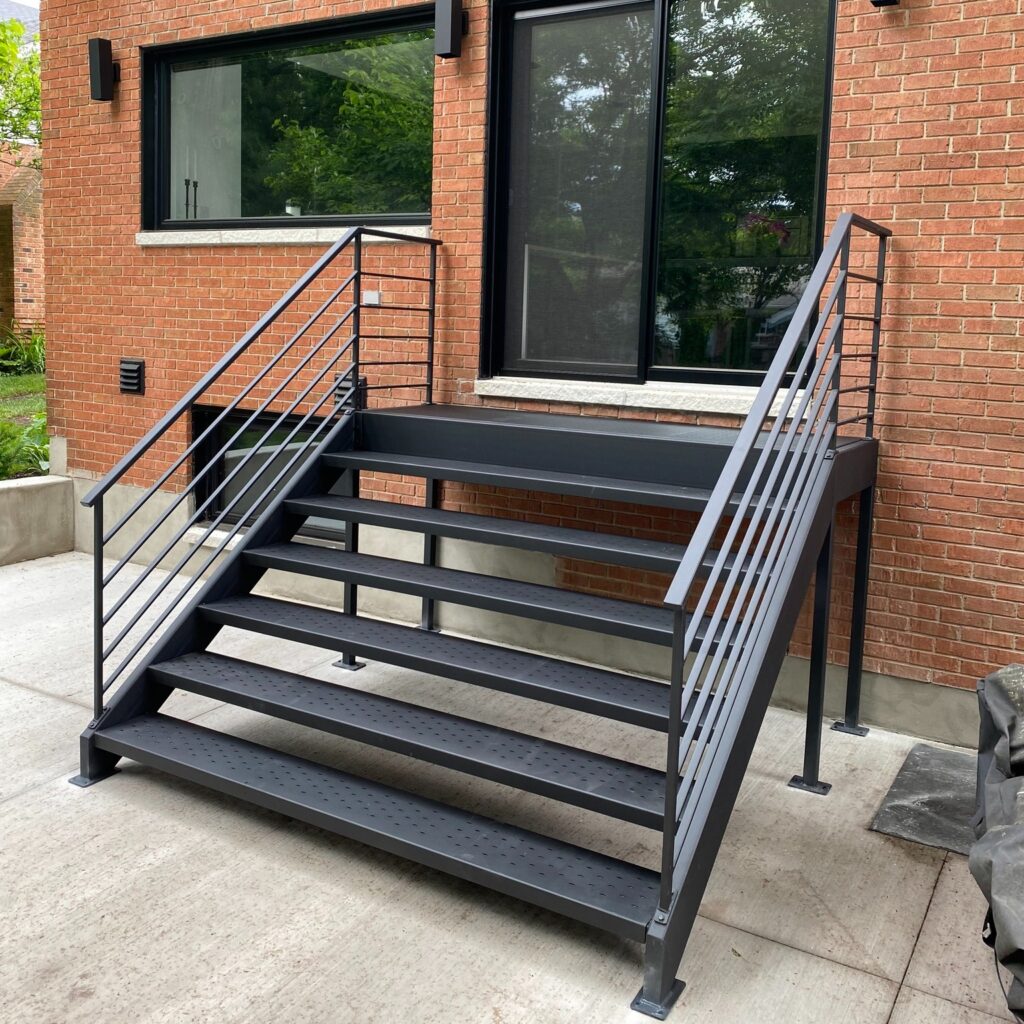 Modern metal tread stairs with black metal railings leading to a building entrance. Metal stair fabricator in Niagara Region.