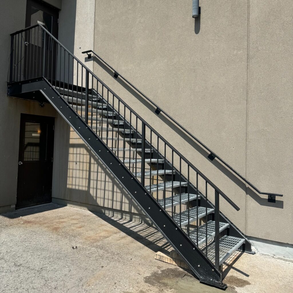 Custom fabricated traditional metal staircase by Dream Ironwork featuring sturdy metal stringers, galvanized steel treads, and a matching handcrafted handrail for durability and classic industrial design.
