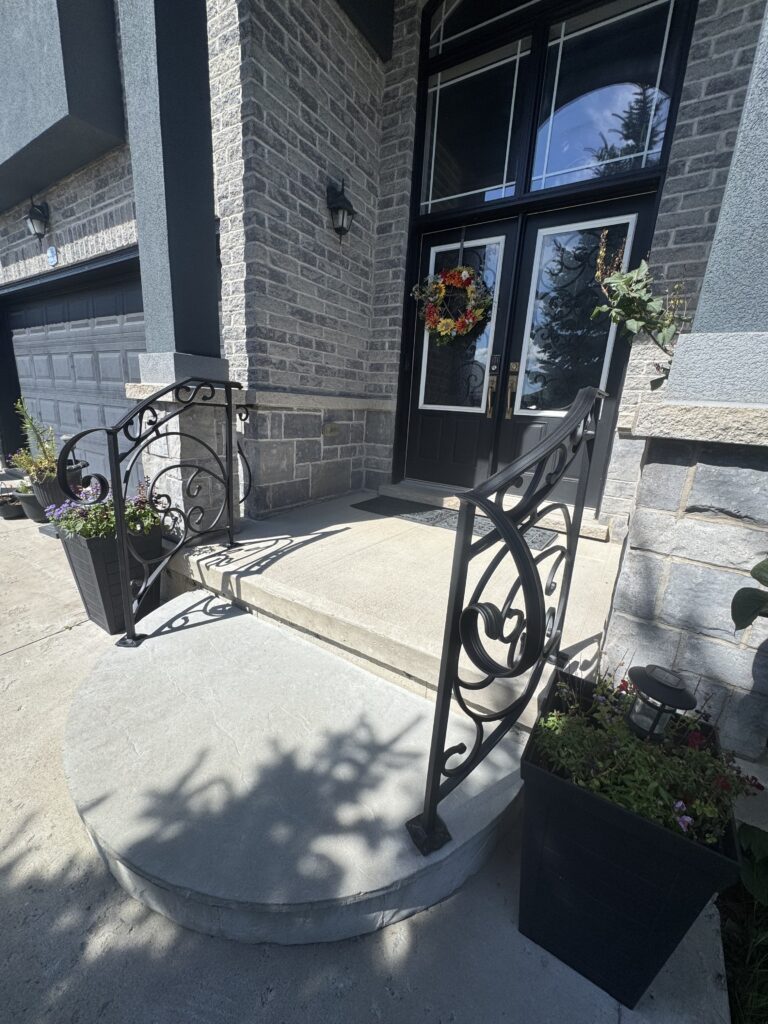 Decorative wrought iron railing on a concrete front entrance, powder coated black.