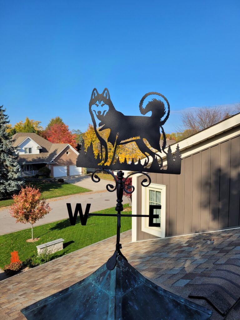 A weather vane atop a building roof with directional indicators. Laser cut weather vane, gift idea. Custom laser cutting.