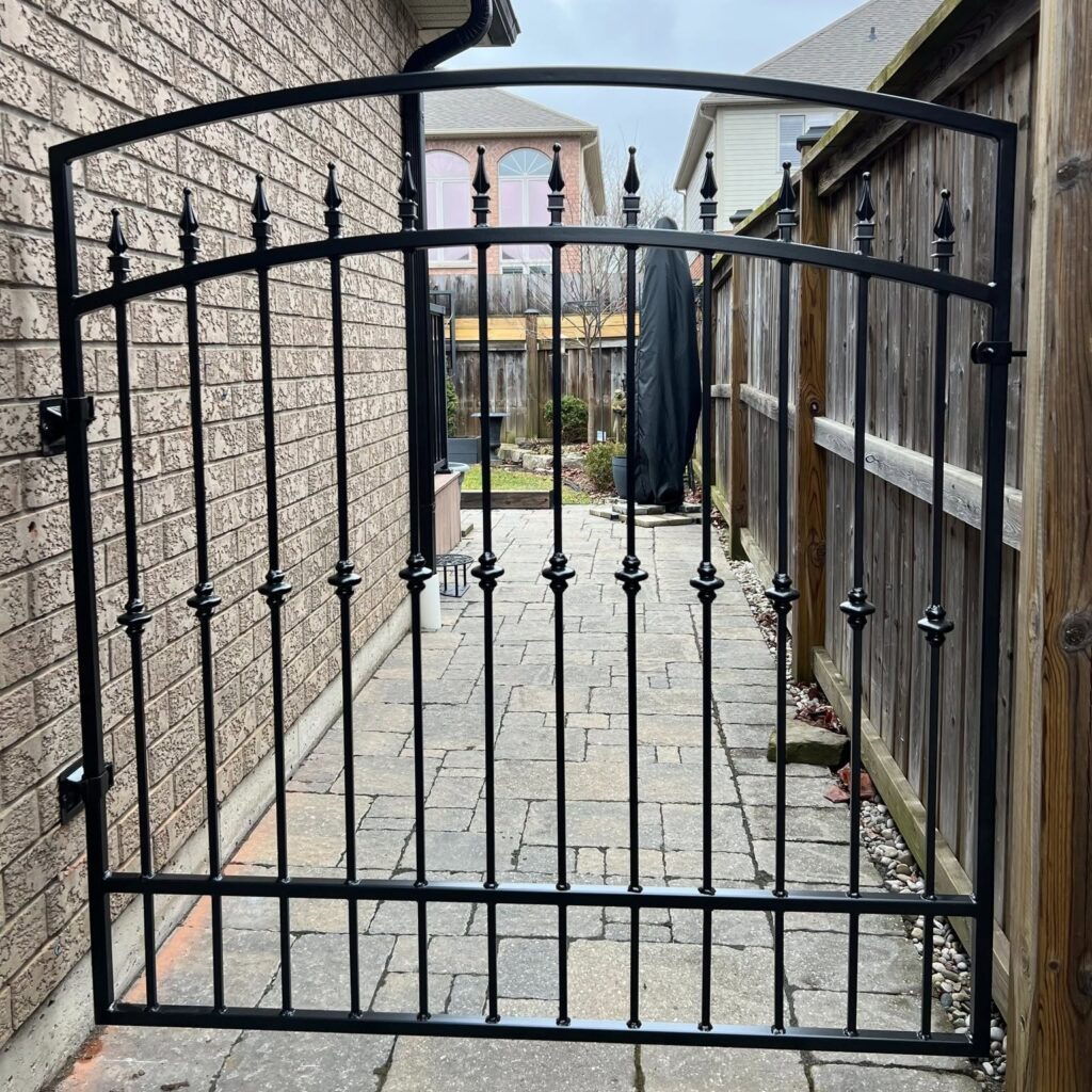 Wrought iron gate mounted to brick and latched off a wooden fence post.
